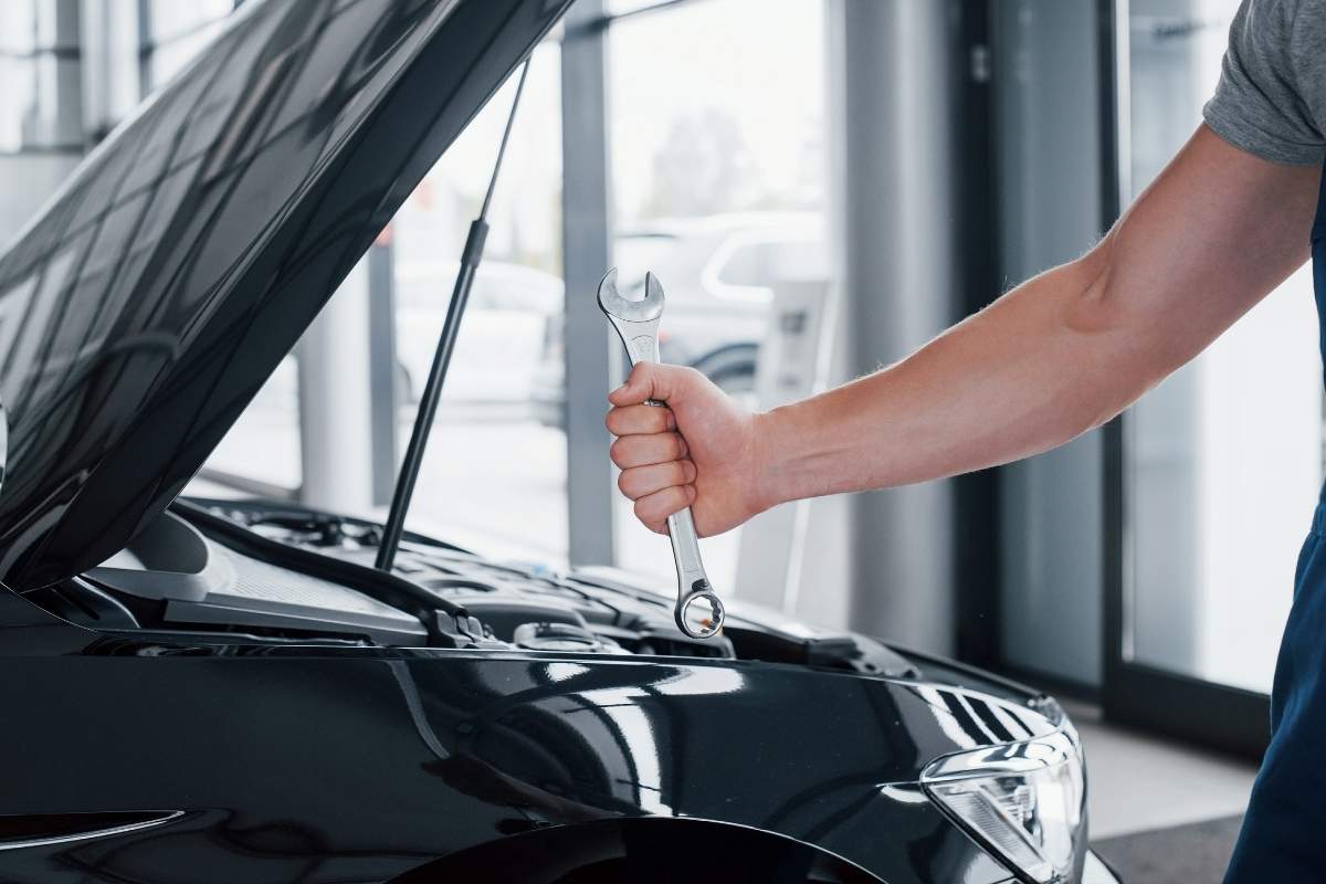 majstor drži ključ za popravljanje automobila u ruci, pored otvorena hauba crnog automobila